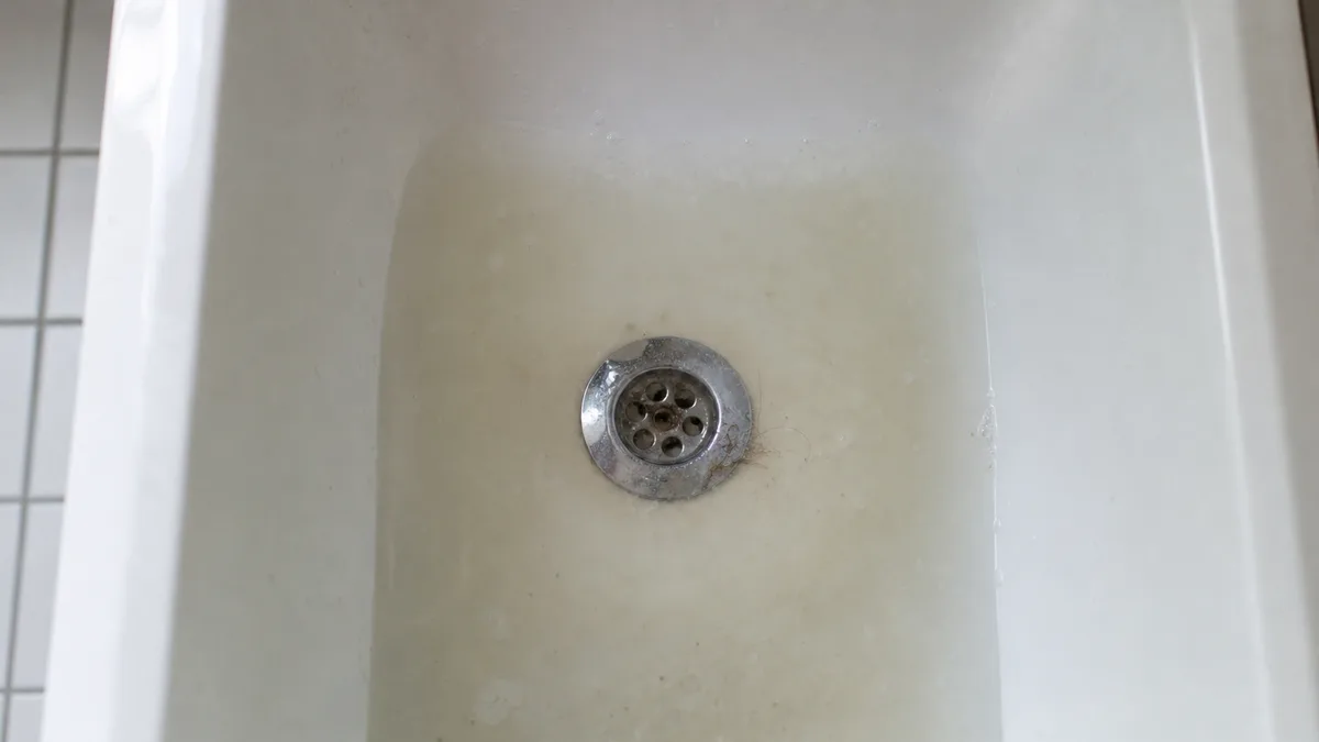 Badewanne von oben, Abflusssieb sichtbar, leicht stehendes Wasser, helles Badezimmer